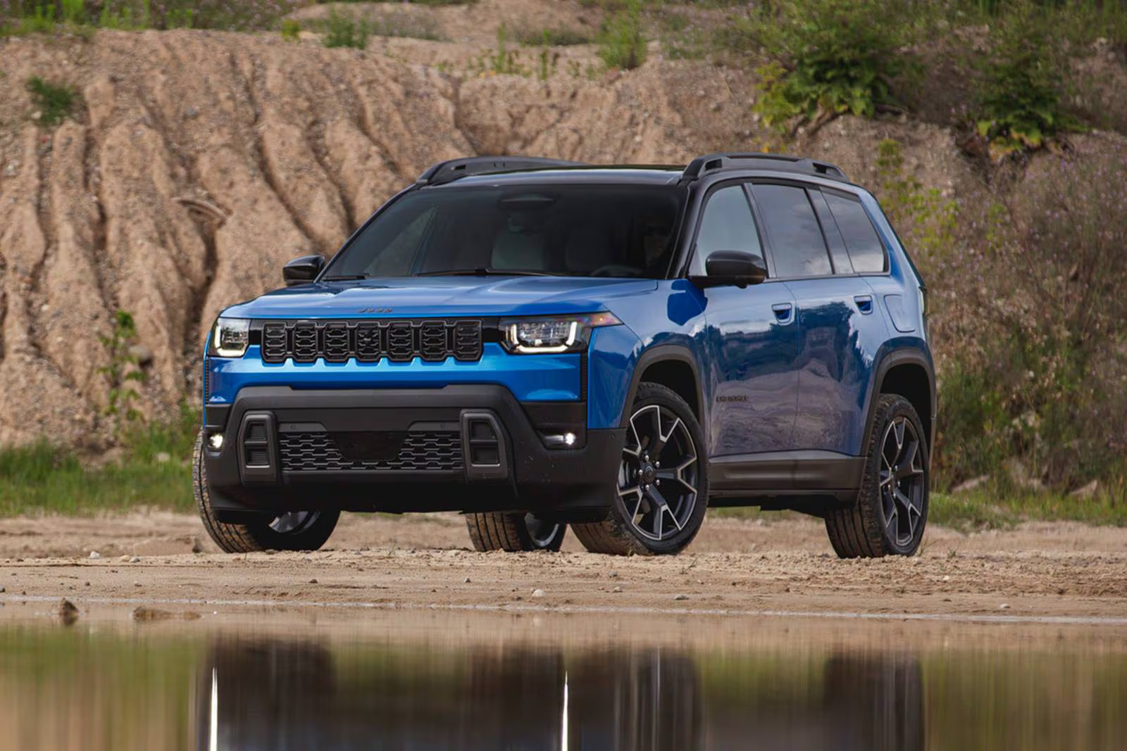 A blue jeep cherokee sitting parked in front of water.