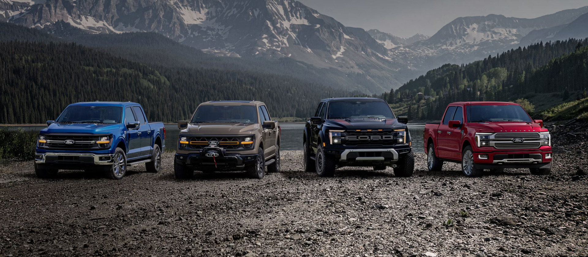 four 2026 ford f-150 trucks parked on gravel near a lake with trees and mountains in the background