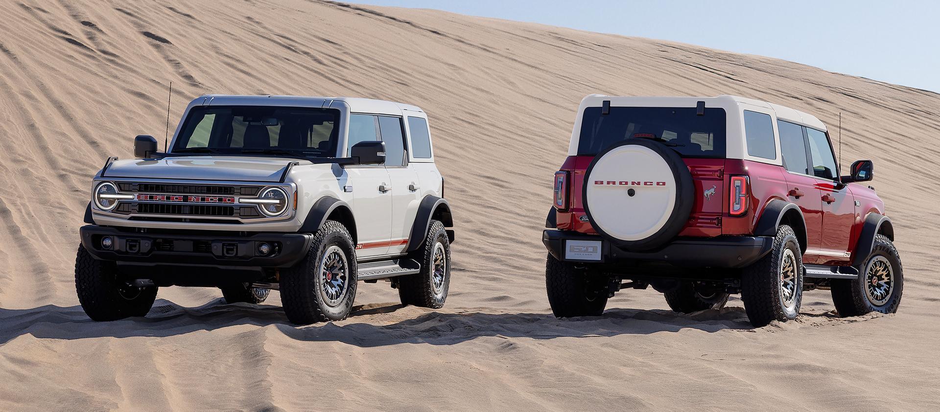 Two ford broncos sitting parked in the desert.
